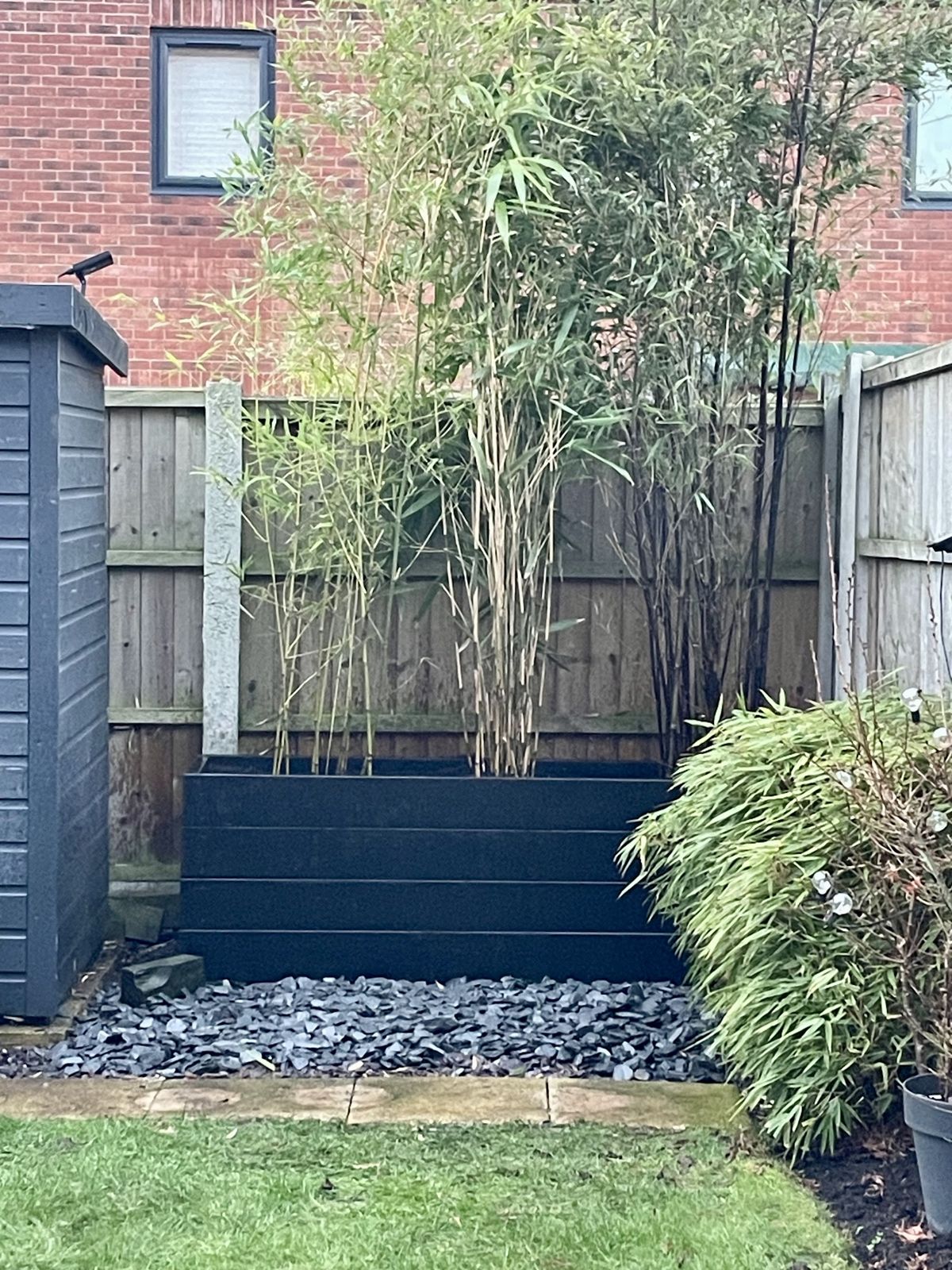 A black sleeper raised bed planted with bamboo and edged in slate chippings