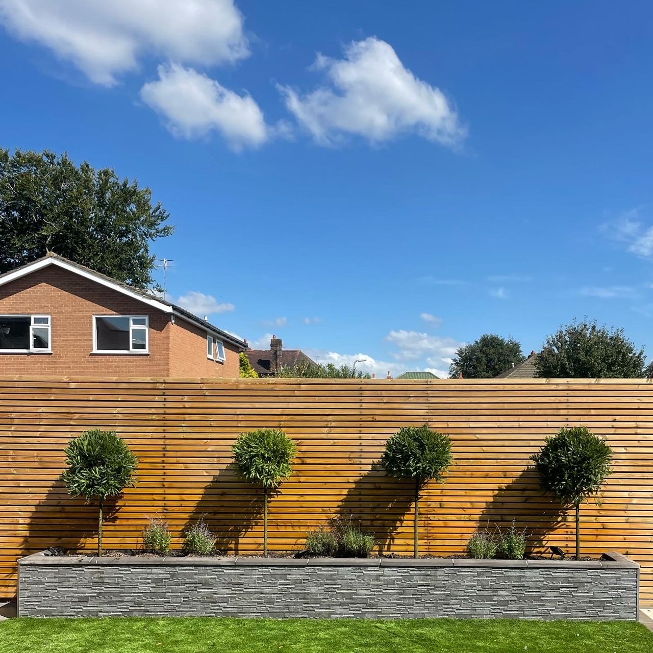 A finished garden makeover: slatted fence, standard trees and a slate faced raised bed