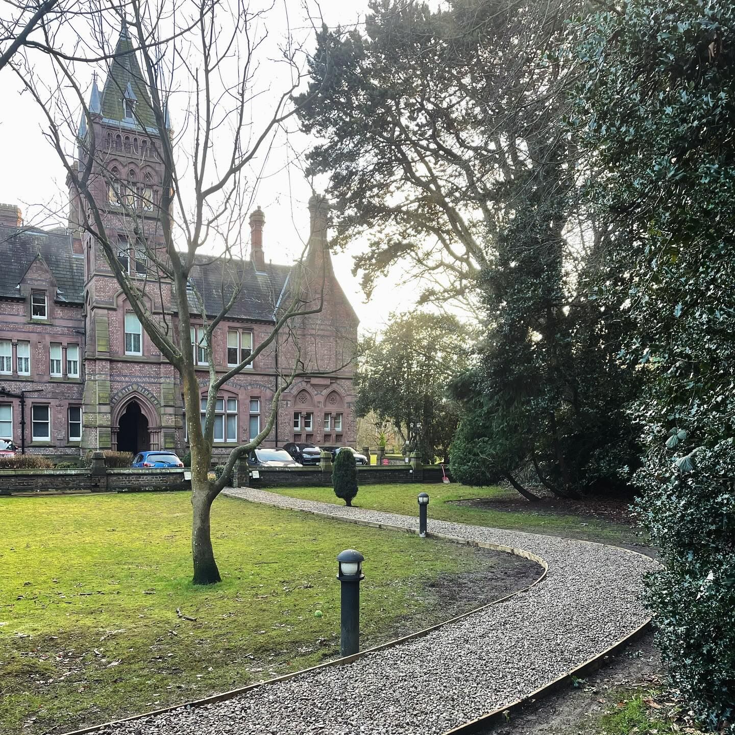 A gravel path curving across the lawn of a red brick Victorian building